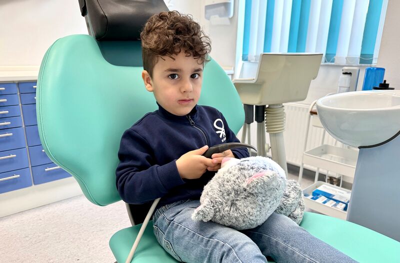 kleiner Junge mit seinem Kuscheltier auf einem Zahnarztstuhl